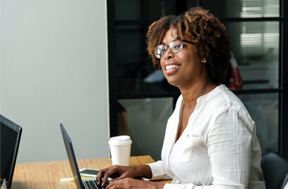 A woman is typing on a laptop while looking ahead and smiling